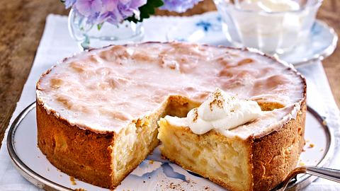 Gedeckter Apfelkuchen aus der Springform mit Zuckerguss, ein Stück herausgeschnitten und mit einem Klecks Sahne bestreut serviert. - Foto: LECKER @ Bauer Media Group