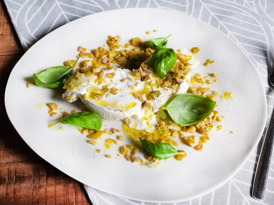 Burrata mit gefrorenen Oliven Burrata liegt auf einem Teller und ist getoppt mit gehackten gefrorenen Oliven, Olivenöl, Basilikum und Zitronenschale