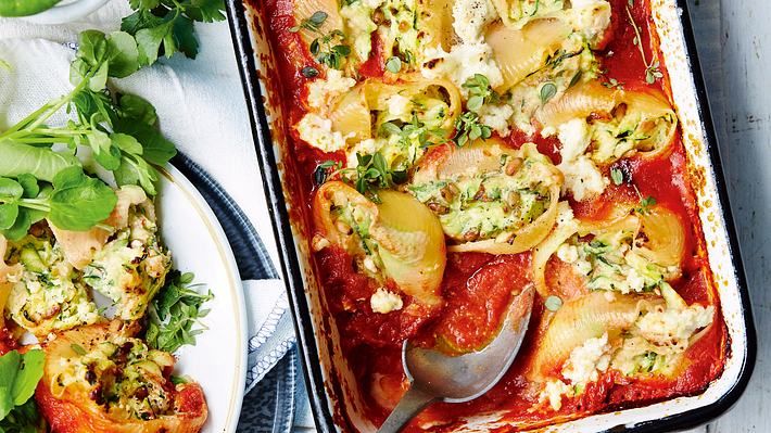 Gefüllte Muschelnudeln in einer Auflaufform mit Tomatensoße und großem Servierlöffel, seitlich auf einem Teller mit frischem Salat serviert.  - Foto: House of Food / Bauer Food Experts KG