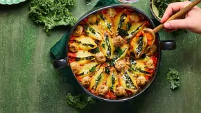 Ofenform mit großen Muschelnudeln, gefüllt mit Grünkohl und Käse, dazu rote Tomatensauce und goldene Käsekruste, auf grünem Untergrund mit passendem grünen Teller daneben. - Foto: LECKER @ Bauer Media Group