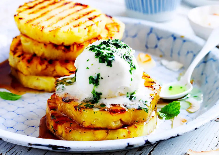 Gegrillte Baby-Ananas mit Kokoseis Minze und Chiliflocken auf einem blau gemusterten Teller.