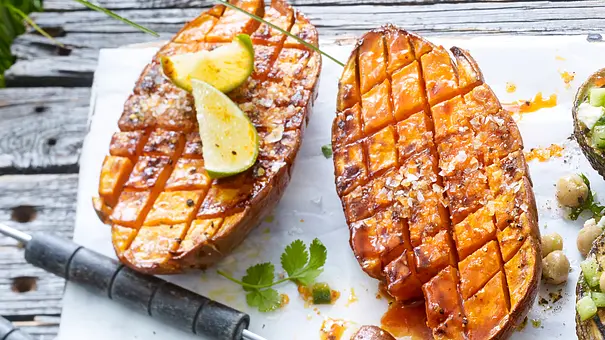 Zwei Hälften gegrillte Süßkartoffel, die Oberfläche netzartig eingeschnitten, zwei Limettenviertel auf einer Hälfte - Foto: LECKER @ Bauer Media Group