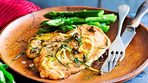 Saftiges Minutenschnitzel mit grünem Spargel auf einem Holzteller mit Besteck - Foto: House of Food / Bauer Food Experts KG