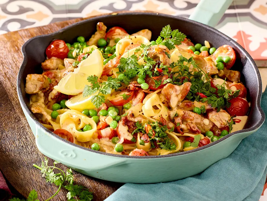 In einer Pfanne ist Geschnetzeltes mit Erbsen, Zitronenscheiben, Tomaten und Kräutern appetitlich angerichtet