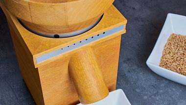 Eine Getreidemühle mit Holzgehäuse und einer Schale voll Dinkelkörner - Foto: iStock/Claudia Nass