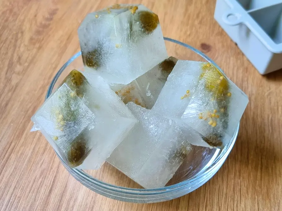Eiswürfel mit Gewürzgurken und Senfkörnern in einer Glasschüssel.