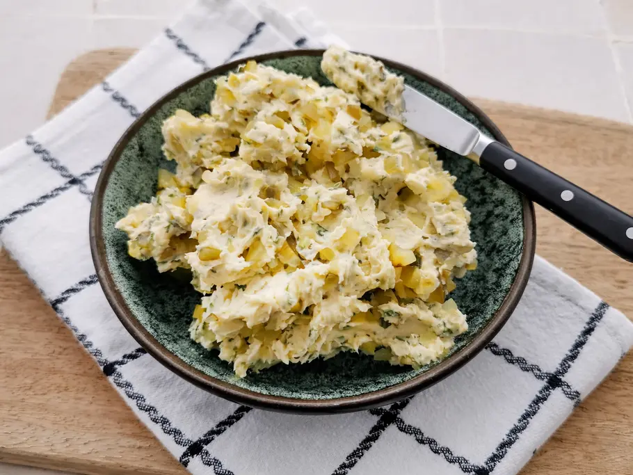 Ein Schale mit stückiger Gewürzgurkenbutter, auf dem Rand liegt ein Buttermesser mit schwarzem Griff