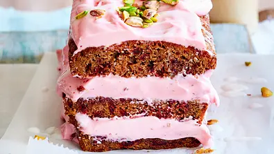 Kastenkuchen mit rosa Frischkäsecreme und Pistazien bestreut, angeschnitten und aufeinander gestapelt auf Backpapier. - Foto: LECKER @ Bauer Media Group