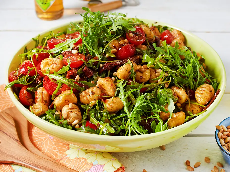 Gnocchi-Salat mit Rucola und getrockneten Tomaten in einer gelben Schüssel serviert.