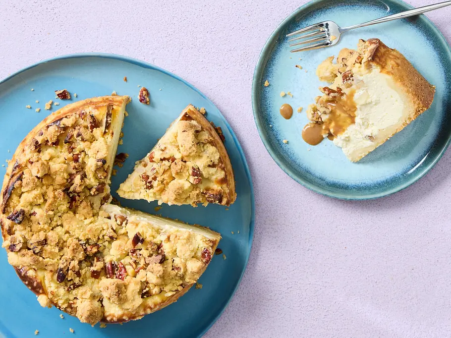 Käsekuchen mit cremiger Füllung und knusprigen Streuseln, angerichtet auf einem blauen Teller, ein Stück separat serviert.