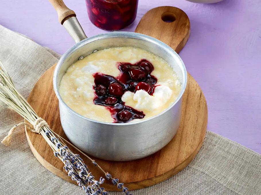 Grießsuppe mit Kirschen befindet sich in einem Stieltopf auf einem Holzuntersetzer.