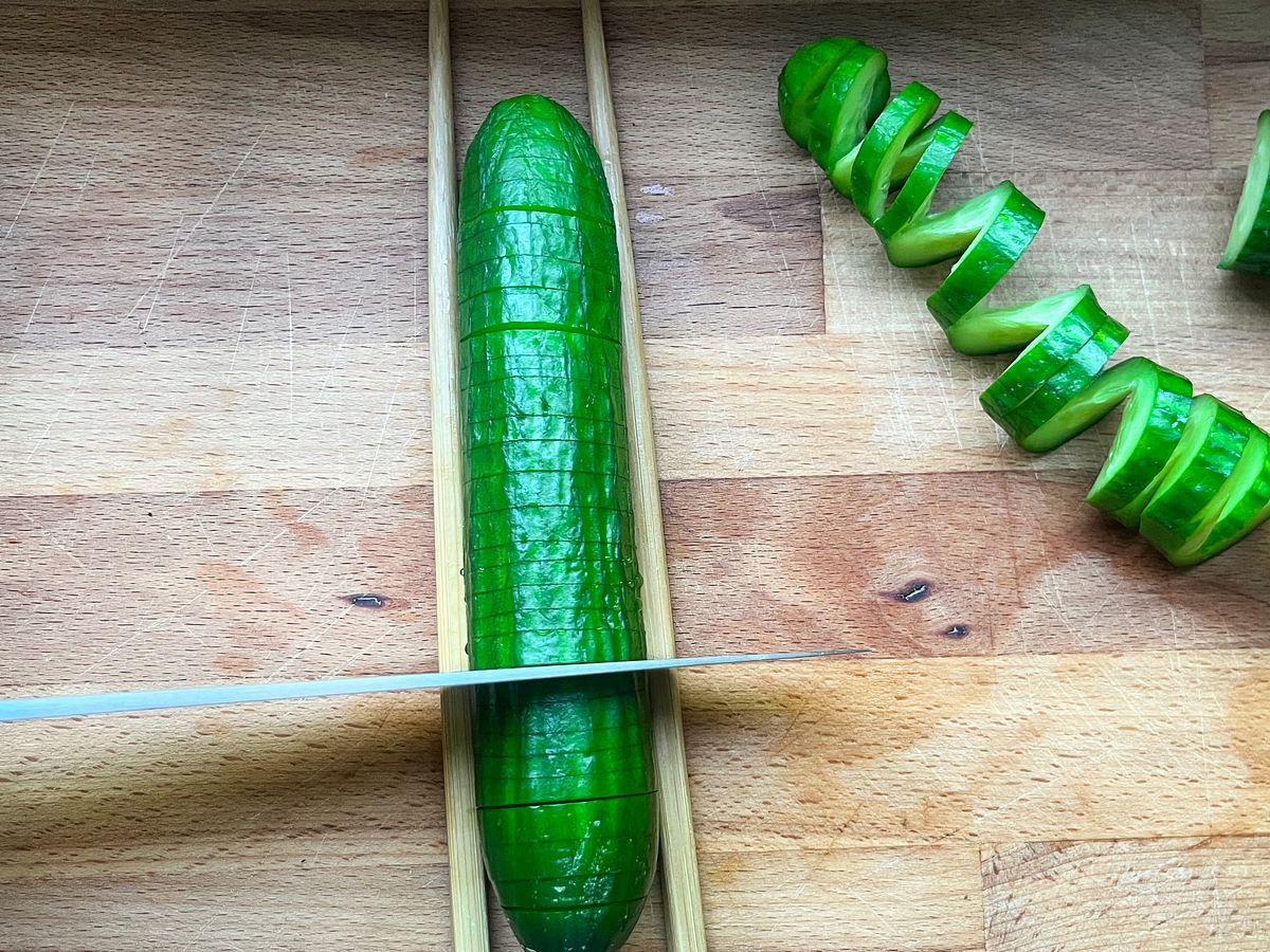 Snack-Gurke wird mit einem Messer zwischen zwei Essstäbchen horizontal im Abstand von 3-5 mm eingeschnitten