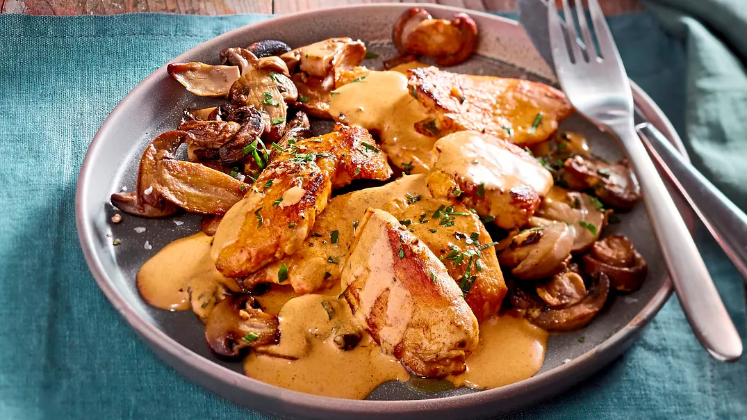 Gebratene Fleischstücke mit Pilzen, cremiger Sauce und gehackten Kräutern liegen auf einem grauen Teller mit Besteck. - Foto: LECKER @ Bauer Media Group Gebratene Fleischstücke mit Pilzen, cremiger Sauce und gehackten Kräutern liegen auf einem grauen Teller mit Besteck. - Foto: LECKER @ Bauer Media Group