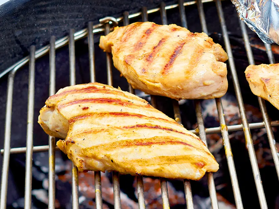 Hähnchenbrüste liegen auf em Rost über der Glut und werden scharf angegrillt.
