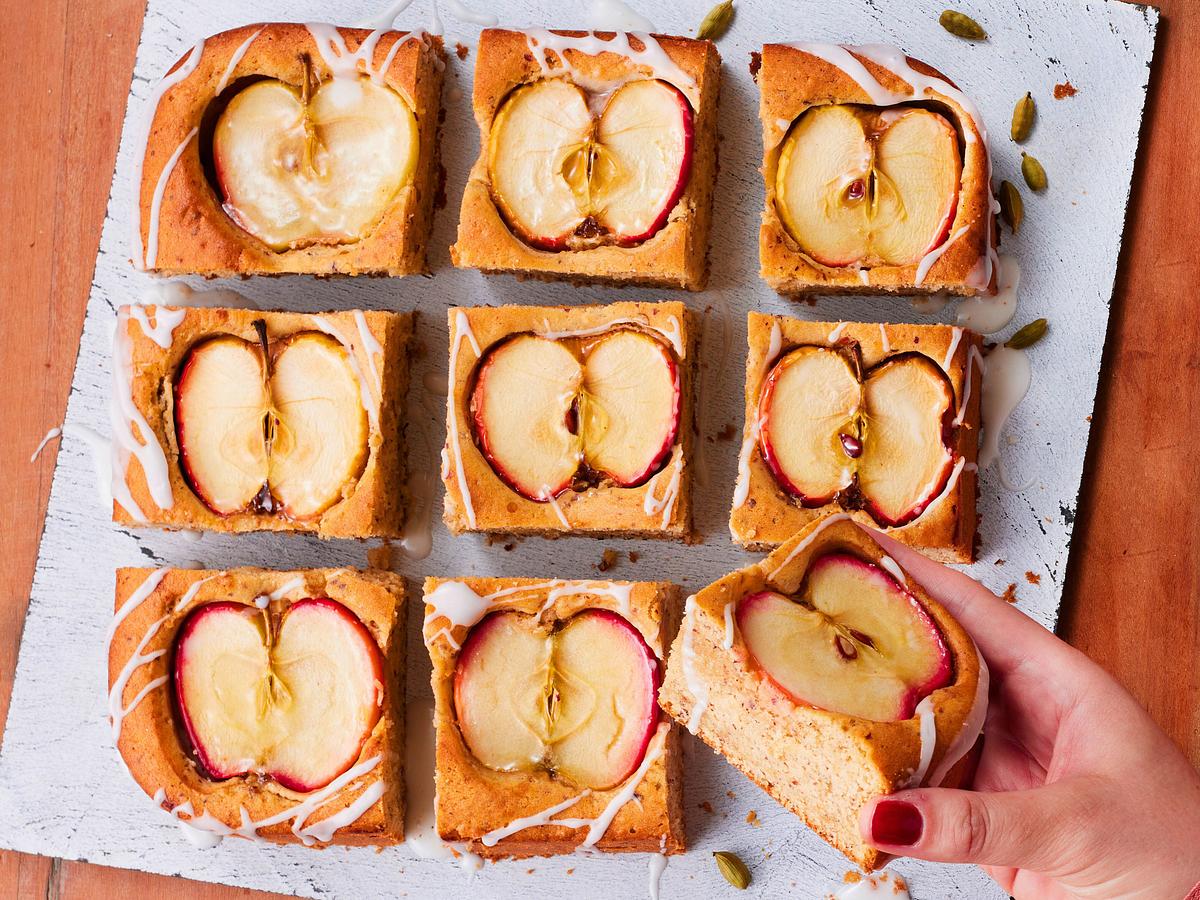 Der Kuchen mit halbierten versunkenen Äpfeln ist in Quadrate geschnitten. Ein Stück wird mit entnommen.