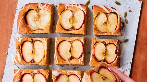 Der Kuchen mit halbierten versunkenen Äpfeln ist in Quadrate geschnitten. Ein Stück wird mit entnommen. - Foto: LECKER @ Bauer Media Group