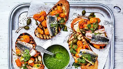 Vier geröstete Crostini belegt mit gelben Kirschtomaten und Sardinenfilets - Foto: Are Media Syndication 