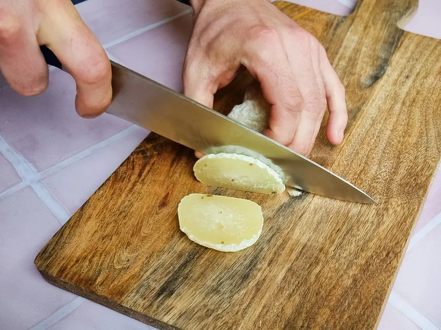 Harzer Käse liegt auf einem Holzbrett und wird in Scheiben geschnitten.