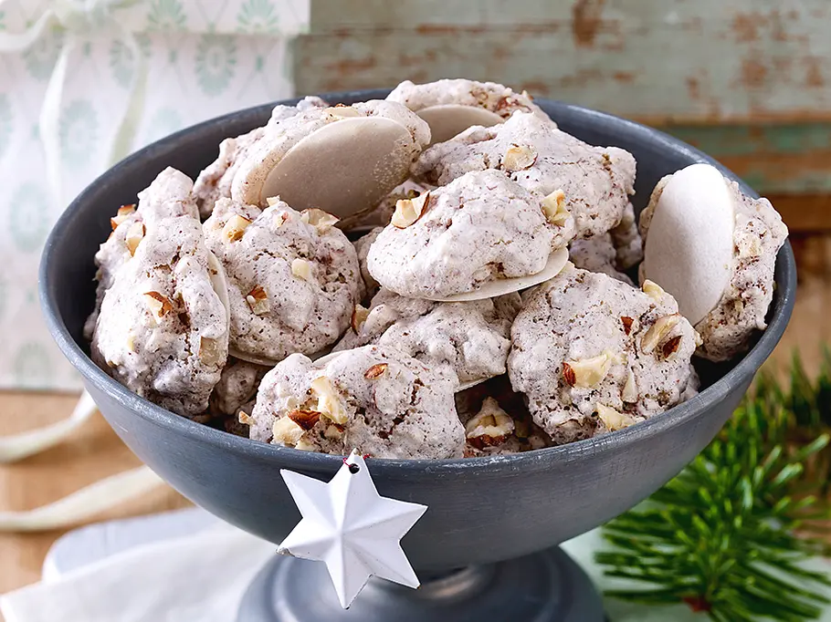 Eine Schüssel mit hellen Makronen, man sieht deutlich Nussstücke, rundherum weihnachtliche Deko
