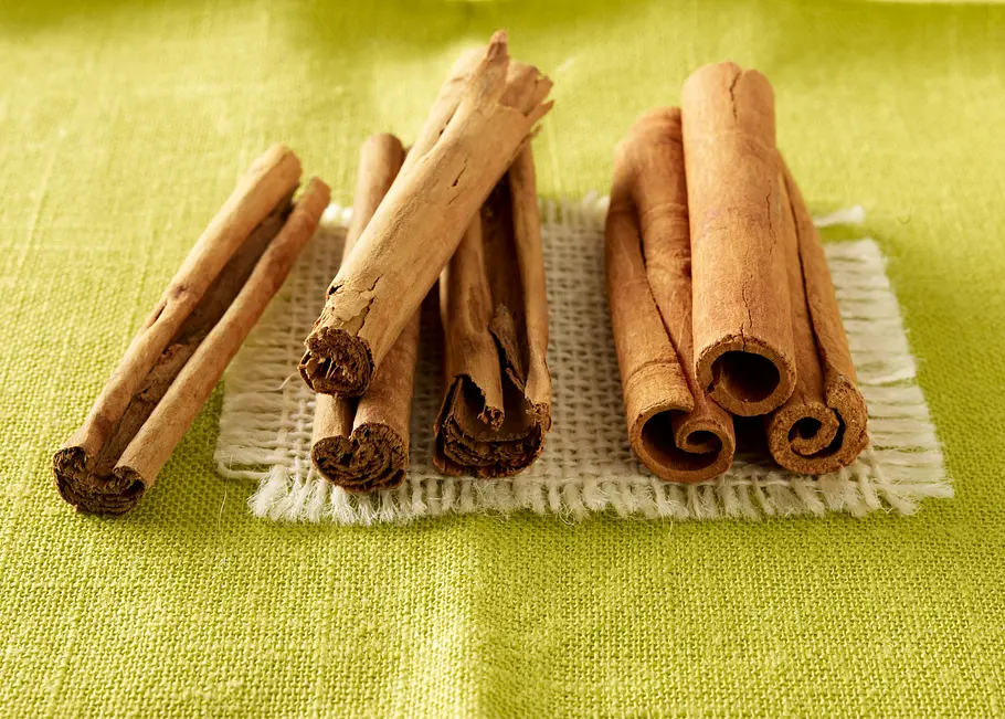 4 blättrige Ceylon-Zimtstangen liegen auf einer grünen Tischdecke neben 3 Cassia-Zimtstangen