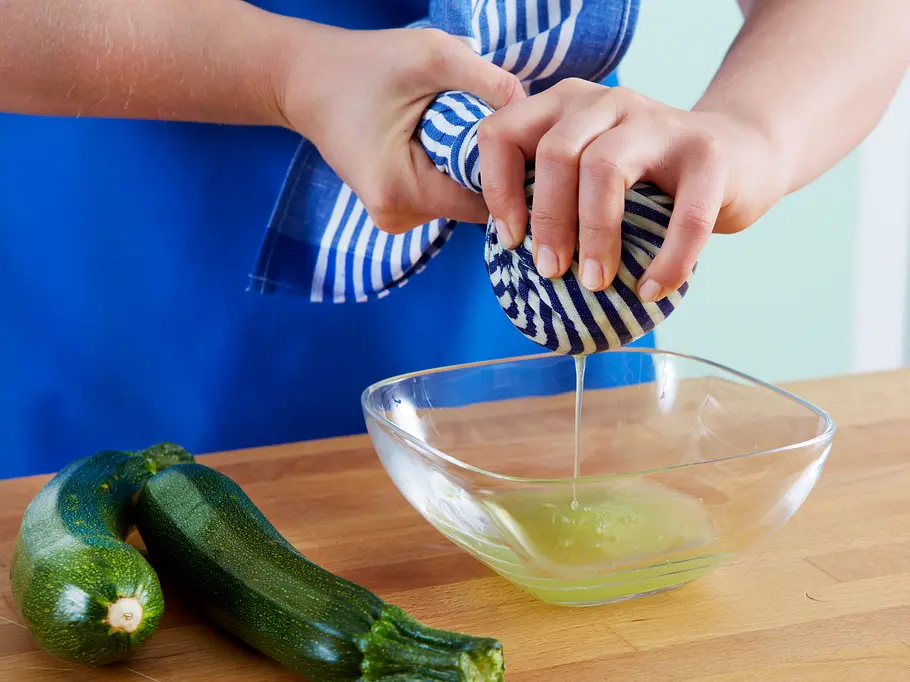 Flüssigkeit aus geraspelten Zucchini wird mit einem Küchentuch ausgepresst, um überschüssiges Wasser zu entfernen.