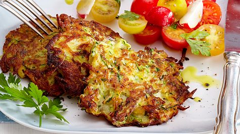 Knusprige Zucchinipuffer mit goldbrauner Kruste, serviert mit einem frischen Tomaten-Radieschen-Salat und Petersilie auf einem weißen Teller.  - Foto: House of Food / Bauer Food Experts KG
