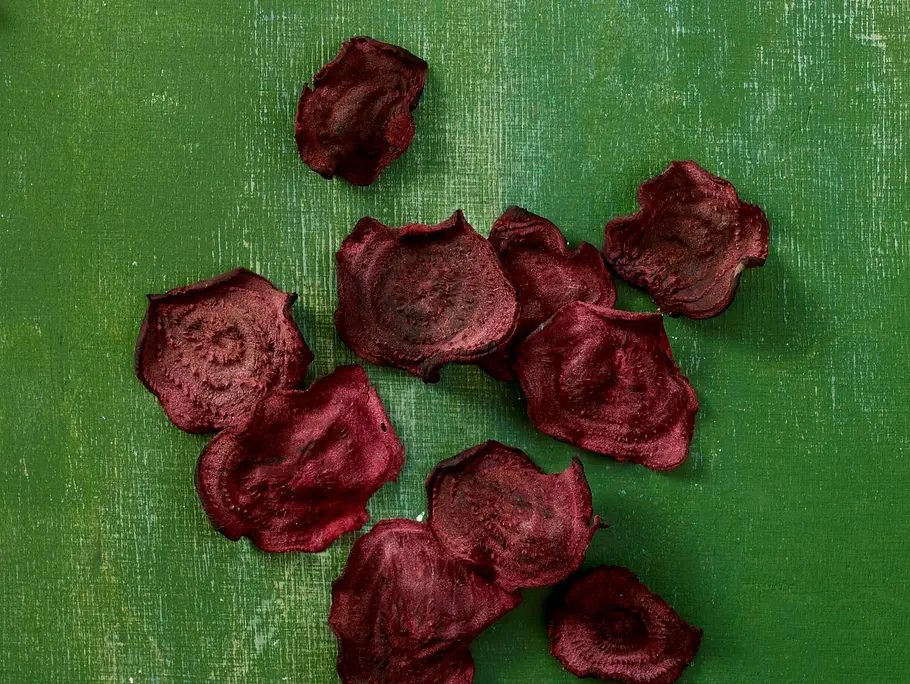 Dünne, knusprige Rote-Bete-Chips mit intensiver violett-roter Farbe, locker auf einem grünen Untergrund angerichtet.