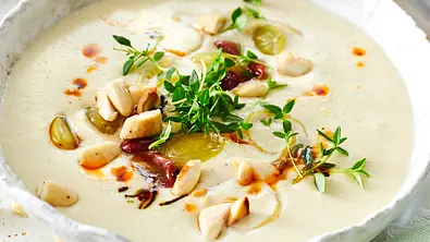 Eine weiße Schüssel mit cremiger Mandelsuppe mit Mandelkernen, Kräutern und rotem Öl als Topping. - Foto: LECKER @ Bauer Media Group