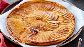 Dünne Tarte mit goldbraun gebackenen, fächerförmig gelegten Apfelscheiben auf buttrigem Teig, serviert auf Backpapier auf einem runden Holzbrett. - Foto: LECKER @ Bauer Media Group Dünne Tarte mit goldbraun gebackenen, fächerförmig gelegten Apfelscheiben auf buttrigem Teig, serviert auf Backpapier auf einem runden Holzbrett. - Foto: LECKER @ Bauer Media Group