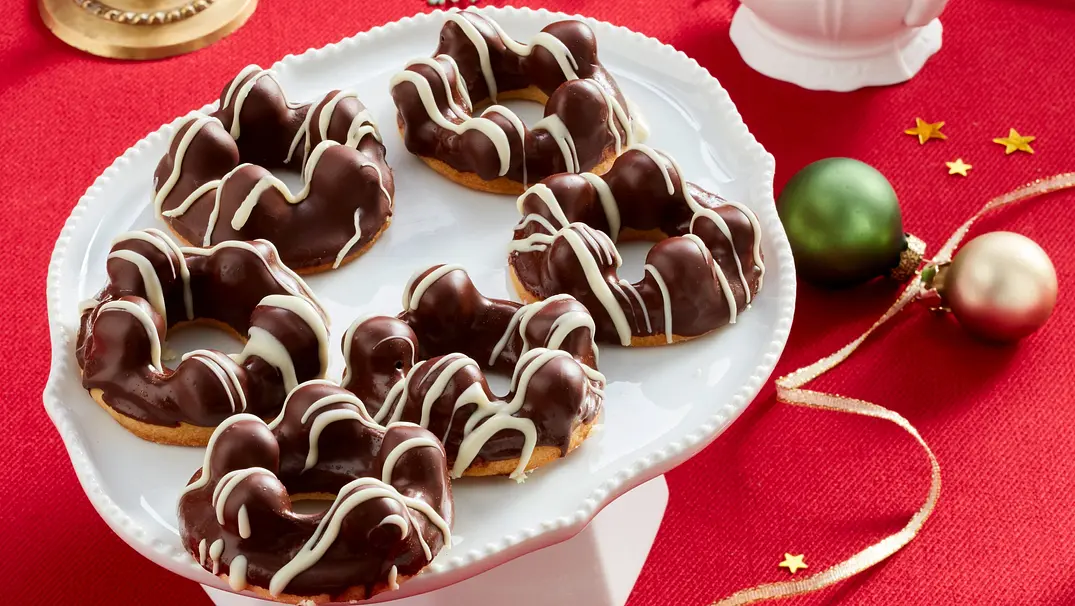 Schokoladenglasierte Haselnussringe, dekoriert mit weißen Schokoladenstreifen, angerichtet auf einer weißen Etagere vor rotem Stoffhintergrund. - Foto: LECKER @ Bauer Media Group Schokoladenglasierte Haselnussringe, dekoriert mit weißen Schokoladenstreifen, angerichtet auf einer weißen Etagere vor rotem Stoffhintergrund. - Foto: LECKER @ Bauer Media Group