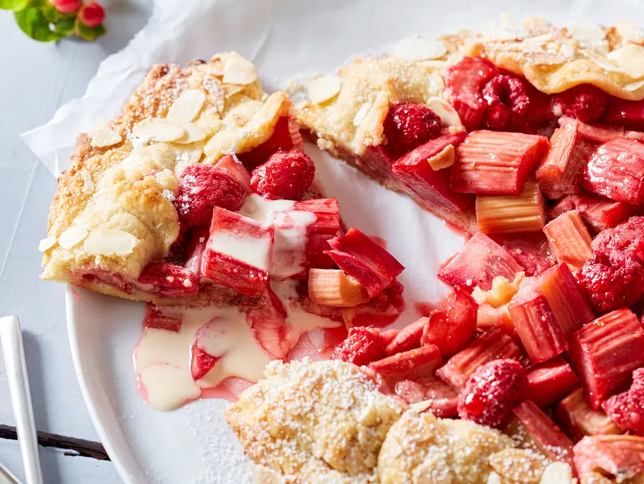 Auf einem weißen Teller liegt eine angeschnittene Rhabarber-Galette, das Stück Galette ist etwas abgerückt und mit Vanillesoße beträufelt