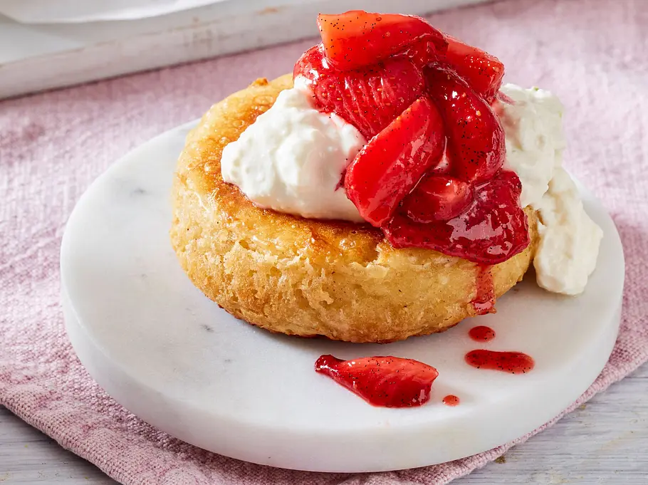 Ein goldbrauner Crumpet auf einem kleinen weißen Marmor-Teller, belegt mit cremigem Ricotta-Hüttenkäse und saftigen Ofen-Erdbeeren.