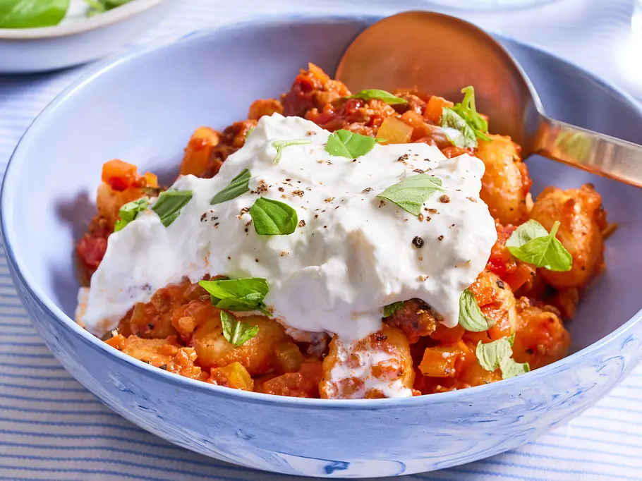 Cremige Gnocchi-Bolognese Gnocchi in cremiger Bolognese-Sauce, serviert in einer blauen Schüssel, garniert mit einem Klecks Frischkäsecreme und frischem Basilikum.