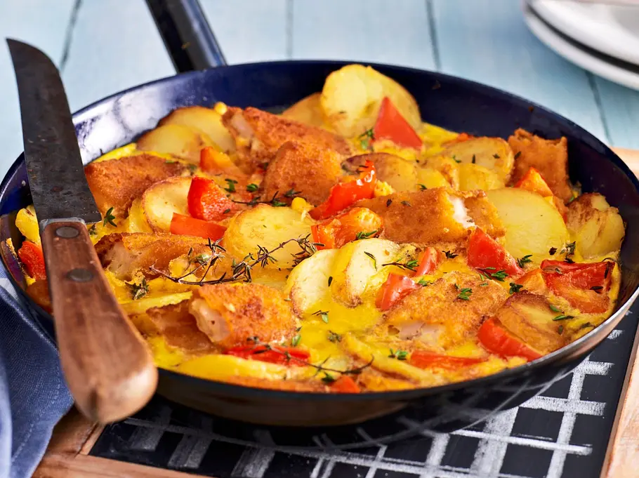 Eine Pfanne gefüllt mich Fischstäbschen und Katroffeln in einer Soße mit Thymian getopped Eine Pfanne gefüllt mich Fischstäbschen und Katroffeln in einer Soße mit Thymian getopped