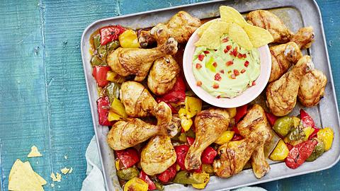 Auf einem Bett aus bunter, kleingeschnittener Ofenpaprika liegen Chickensticks und in der Mitte trohnt eine kleine Schale mit grüner Guacamole und Tortillachips - Foto: House of Food / Bauer Food Experts KG