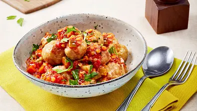 In einer weißen Keramikschale sind Knödel in einer roten Soße mit Linsen und grüner Petersilie angerichtet - Foto: LECKER @ Bauer Media Group
