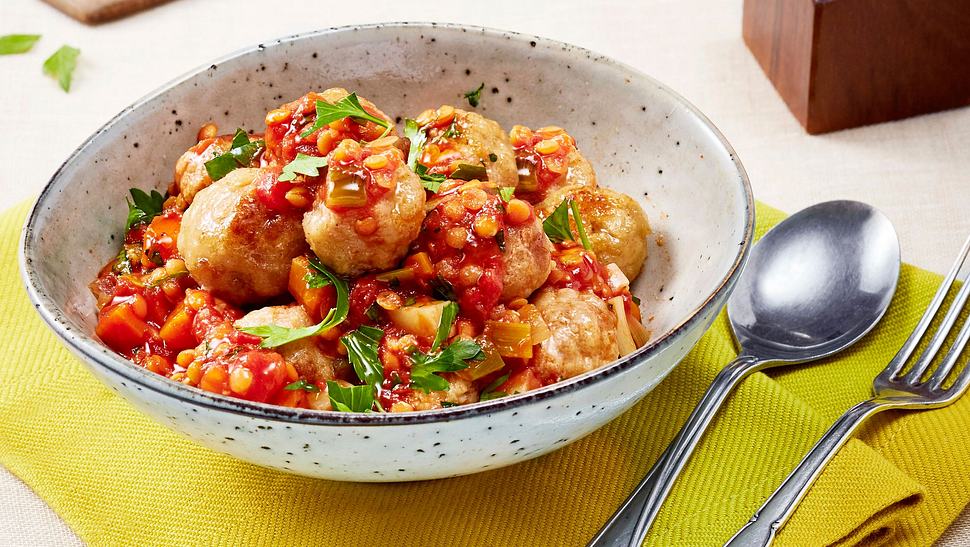 In einer weißen Keramikschale sind Knödel in einer roten Soße mit Linsen und grüner Petersilie angerichtet - Foto: House of Food / Bauer Food Experts KG