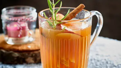 Heißer Apfelwein im Glas, eine Zimtstange, ein Rosmarinzweig und Apfelscheibchen im Glas als Deko. - Foto: LECKER @ Bauer Media Group