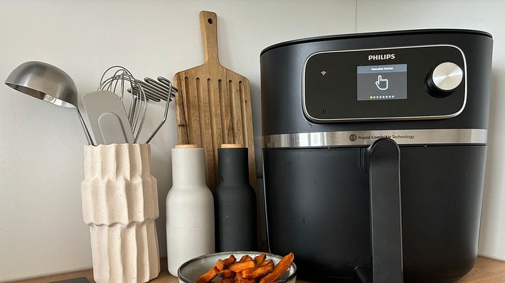 Ein Airfryer steht neben einer Schüssel Süßkartoffelpommes und Küchenutensilien auf einer Küchenzeile - Foto: LECKER.de