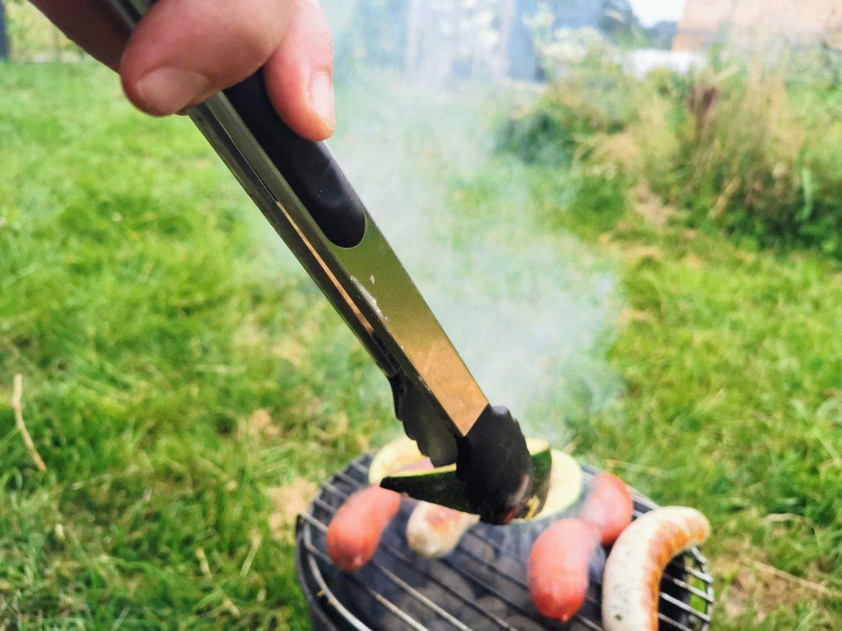 Kürbis und Würstchen werden auf einem Holzkohlegrill mit der Henssler Grillzange gewendet.
