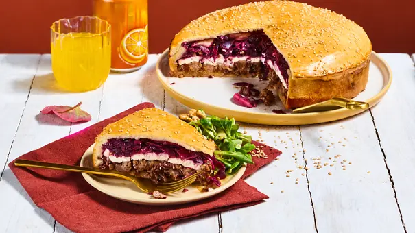 Ein angeschnittener Riesen-Burger mit Sesamkruste und Rotkohl steht neben einem gelben Getränk und einer Dose. - Foto: StockFood Studios / Meike Bergmann Ein angeschnittener Riesen-Burger mit Sesamkruste und Rotkohl steht neben einem gelben Getränk und einer Dose. - Foto: StockFood Studios / Meike Bergmann