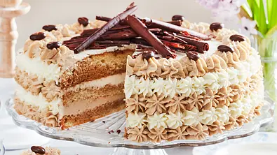 Eine angeschnittene Herrencreme-Torte mit drei Biskuit-Schichten auf einer Tortenplatte - Foto: LECKER @ Bauer Media Group