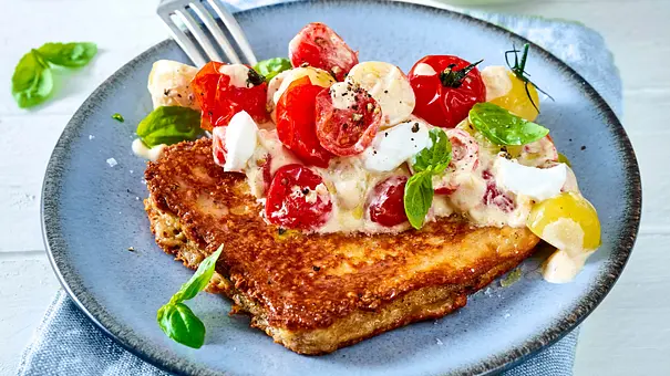 Auf einem blauen Teller liegt geröstetes Brot mit roten und gelben Tomaten, weißem Käse, cremiger Sauce und Basilikum. - Foto: LECKER @ Bauer Media Group