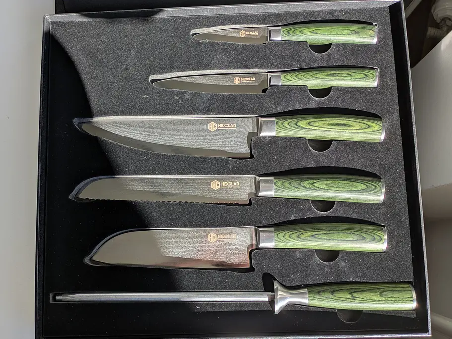 Das HexClad Essential Messerset mit sechs Messern und grünen Griffen liegt ordentlich in einer schwarzen Geschenkbox.