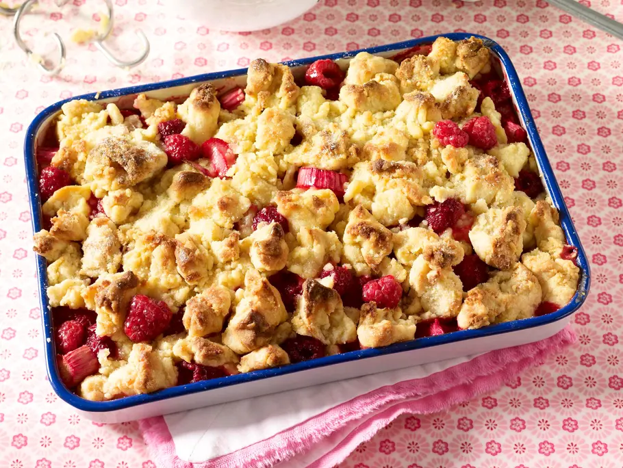 Himbeer-Rhabarber-Crumble Rezept Auflaufform mit Himbeer-Rhabarber-Crumble, bedeckt mit goldbraunen Streuseln; roten Himbeeren und Rhabarberstücken.