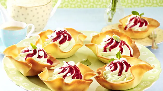 Auf einem dekorativen Teller stehen knusprige Gebäckschalen, die mit einer hellen Creme und fruchtigem roten Soßenspiegel garniert sind – bereit zum Servieren beim Kaffeeklatsch. - Foto: LECKER @ Bauer Media Group Auf einem dekorativen Teller stehen knusprige Gebäckschalen, die mit einer hellen Creme und fruchtigem roten Soßenspiegel garniert sind – bereit zum Servieren beim Kaffeeklatsch. - Foto: LECKER @ Bauer Media Group