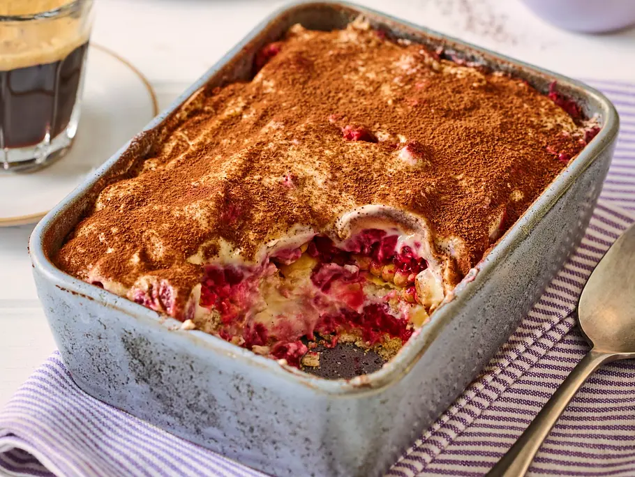 Tiramisu mit Butterkeksen und Himbeeren Tiramisu mit einer Schicht Kakao, frischen Himbeeren und Butterkeksen in einer rechteckigen Auflaufform auf einem gestreiften Tuch.