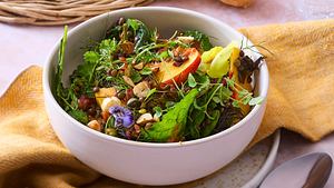  Ein bunter Blattsalat mit Blüten, Nüssen, Belugalinsen, Nekatarinenscheiben und Tomatendressing in einer weißen Schüssel - Foto: House of Food / Bauer Food Experts KG