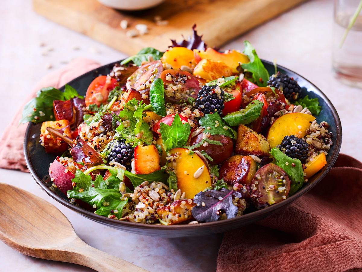In einer Schüssel angerichteter Salat, mit Halloumi-Pfirsich mit Quinoa. Das ganze ist mit einem Dressing durchzogen mit Körner, Salat und Brombeeren drauf.