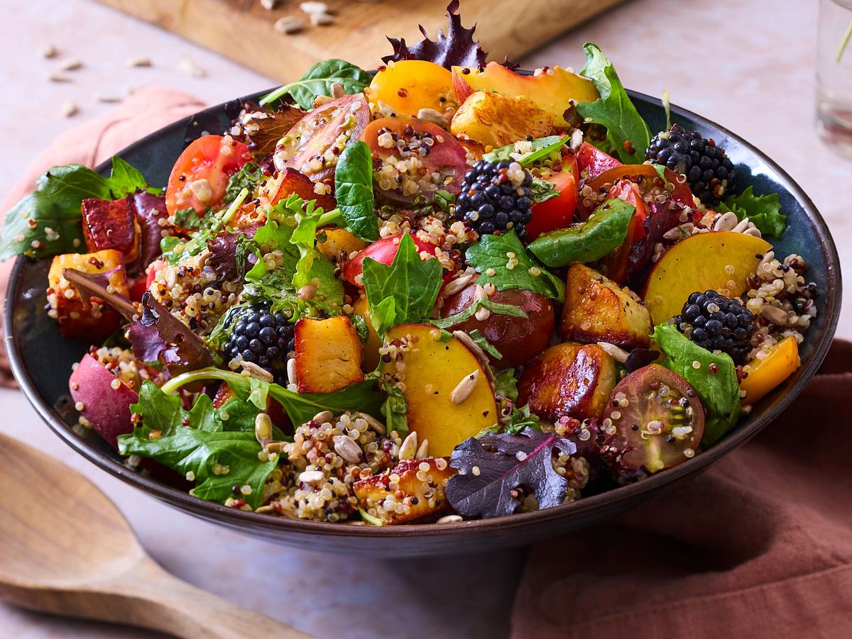 In einer Schüssel angerichteter Salat, mit Halloumi-Pfirsich mit Quinoa. Das ganze ist mit einem Dressing durchzogen mit Körner, Salat und Brombeeren drauf.